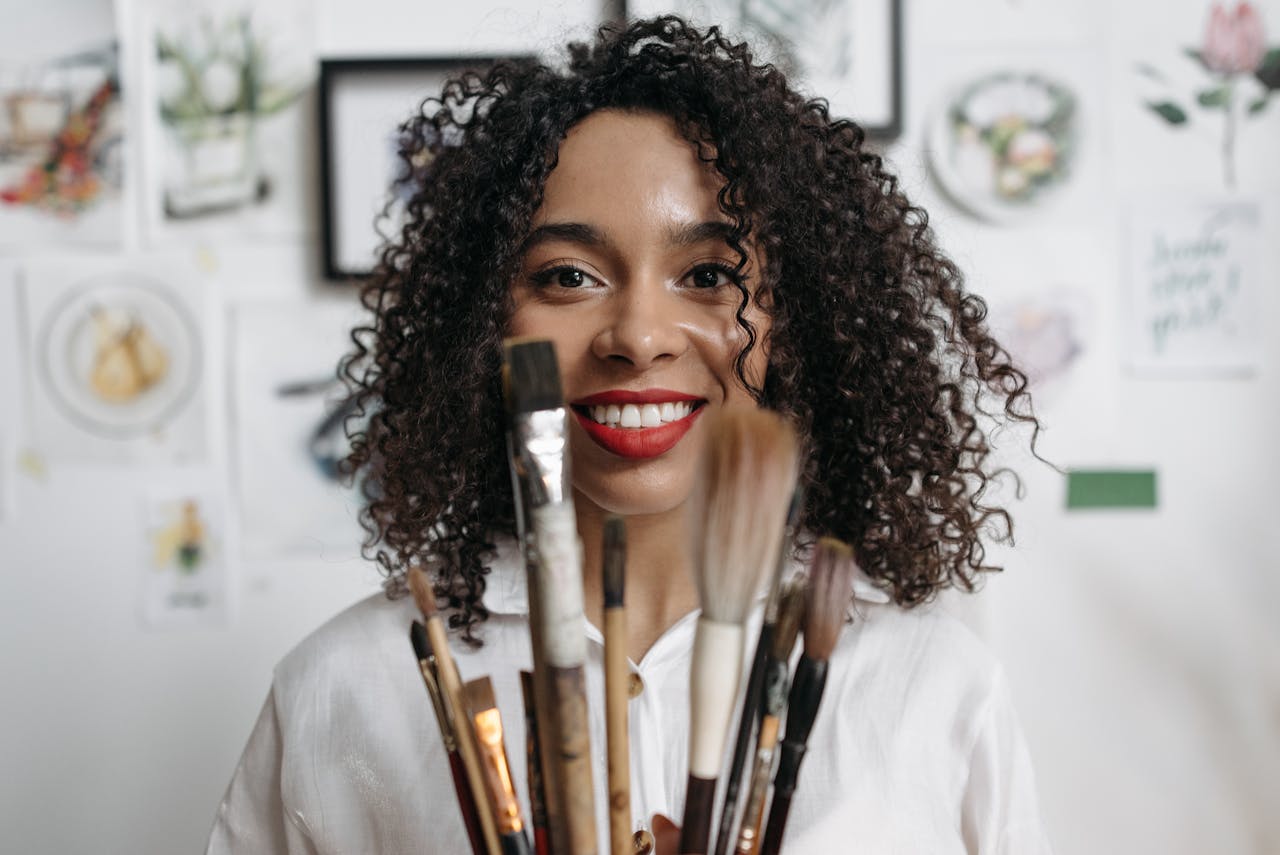 Portrait of a cheerful female artist holding paintbrushes indoors.